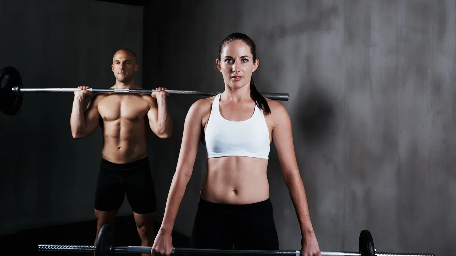 Person som tränar med skivstång i ett gym med flera träningsstationer i bakgrunden